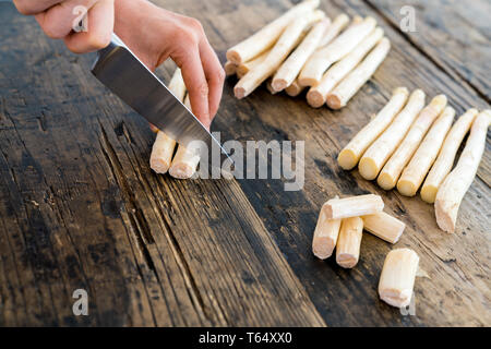 Cuoca il taglio e la preparazione di asparagi bianchi con un coltello affilato su un rustico di una superficie di legno Foto Stock