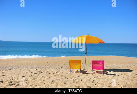 Due pittoresca spiaggia di sedie e ombrellone con blu acqua di mare sullo sfondo. Nazare Beach, Portogallo Foto Stock