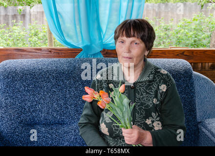 Donna anziana, seduti in giardino, con un bouquet di tulipani rossi, per la madre di vacanza Foto Stock