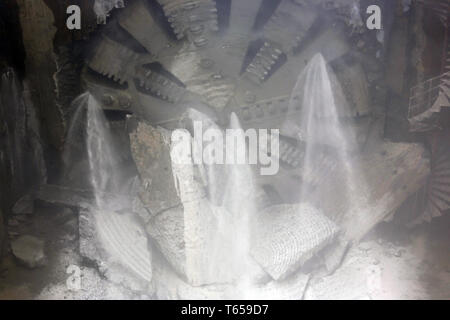 Macchina di foratura di gallerie testata anteriore elemento è visto rotante su una stazione della metropolitana in costruzione. La polvere e l'acqua. Foto Stock