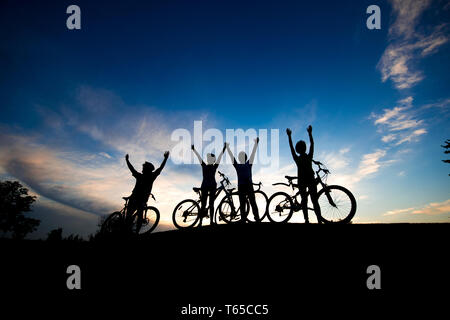 Quattro i ciclisti con le mani alzate al tramonto. Foto Stock