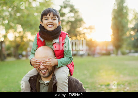 Ritratto giocoso figlio a cavallo sulle spalle dei padri in autunno park Foto Stock