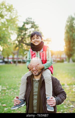 Ritratto giocoso figlio a cavallo sulle spalle dei padri in autunno park Foto Stock