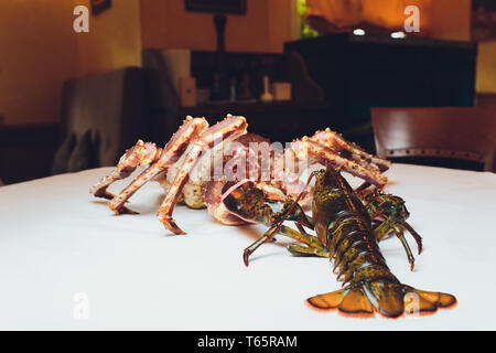 Re granchi e aragoste vive uno opposto all'altro su uno sfondo bianco. giacente sul tavolo contro lo sfondo del ristorante Foto Stock