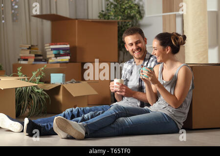 Coppia felice casa mobile di appoggio e di parlare seduto sul pavimento di bere il caffè Foto Stock