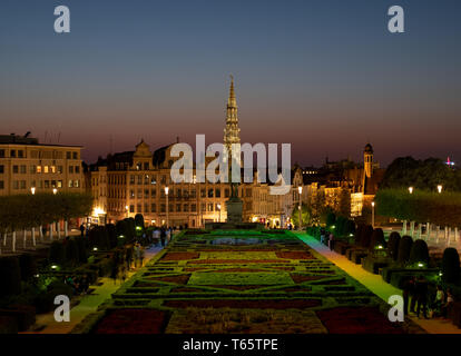 La guglia di Bruxelles Municipio sulla Grand Place è visto all'orizzonte, fotografata da sopra gli illuminati Mont des Arts giardini al tramonto. Foto Stock