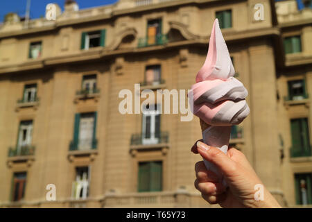 Donna di mano che regge due-tono Soft servire il gelato a forma di cono con sfocate edificio d'epoca nel contesto Foto Stock