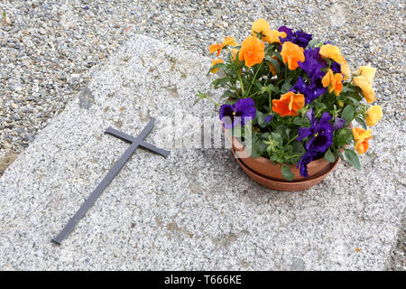 Croix et pot de fleurs sur une pierre tombale. Foto Stock