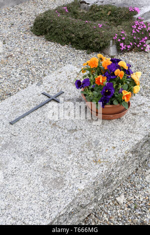Croix et pot de fleurs sur une pierre tombale. Foto Stock