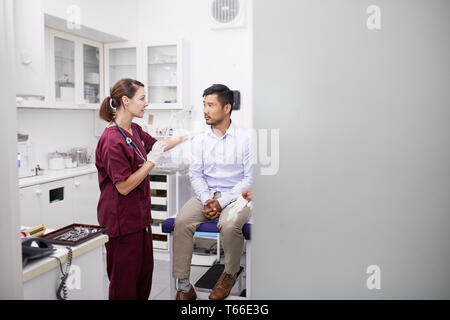Medico donna parlando con paziente di sesso maschile in clinica sala esame Foto Stock