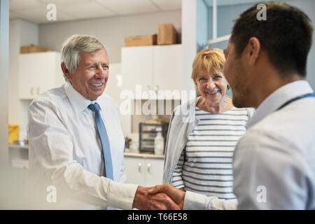 Medico stringono le mani con coppia senior in clinica sala esame Foto Stock