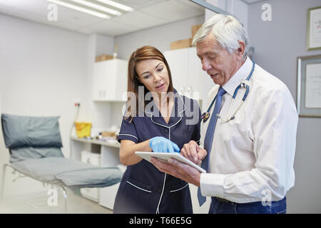 Medico e infermiere con tavoletta digitale parlando in clinica sala esame Foto Stock