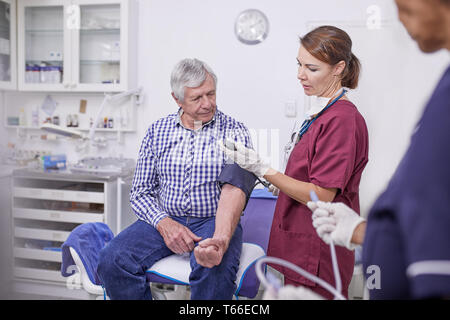 Medico controllando la pressione del sangue del paziente senior in clinica sala esame Foto Stock