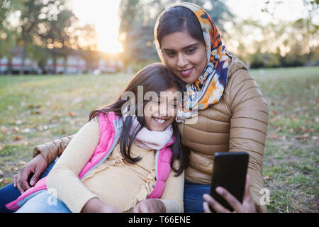 Mamma musulmana in hijab tenendo selfie con la figlia nel parco di autunno Foto Stock