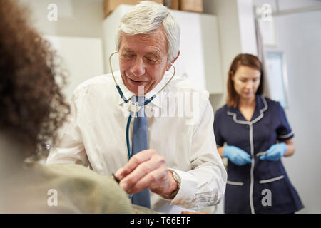 Medico utilizzando uno stetoscopio sul client in clinica Foto Stock