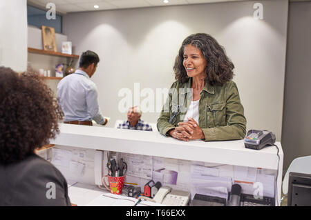 Donna sorridente il check in presso la reception della clinica Foto Stock