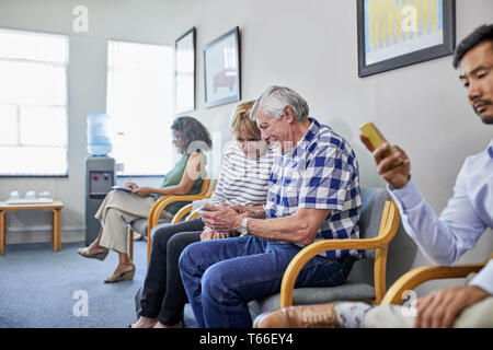 Coppia senior utilizzando smart phone in clinica in sala d'attesa Foto Stock