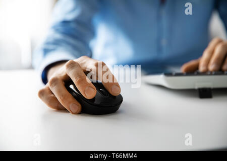 Collare bianco lavoro - uomo al lavoro con computer desktop in ufficio closeup di mano facendo clic su mouse Foto Stock