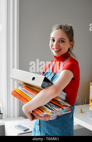 Ritratto fiducioso femmina giovane studente di college che trasportano pila di libri e di legante Foto Stock