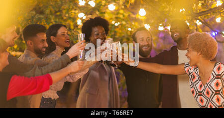 Amici celebrando la tostatura a champagne dinner party in giardino Foto Stock