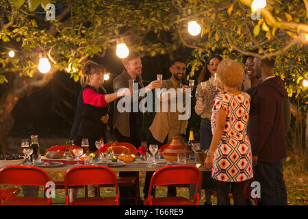 Amici celebrando la tostatura a champagne dinner party in giardino Foto Stock