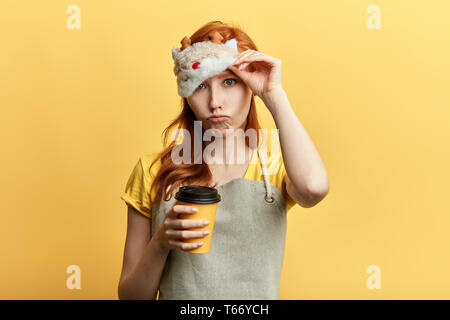 Stanco di sleepy ragazza ha espressione triste, detiene tazza monouso di bevanda, mattina con caffè. Buongiorno, isolato sfondo giallo,stanchezza Foto Stock