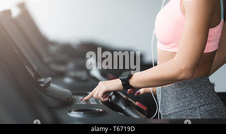 Ragazza regolando la velocità sul tapis roulant, facendo cardio allenamento in palestra, raccolto Foto Stock