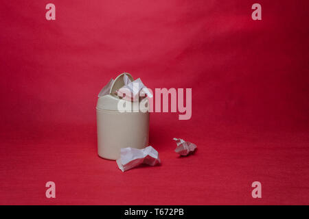 Luce trash bin su uno sfondo di colore rosso. Primo piano della sgualciti fogli di carta. Il concetto di riciclaggio ambientale dei rifiuti di carta. Foto Stock