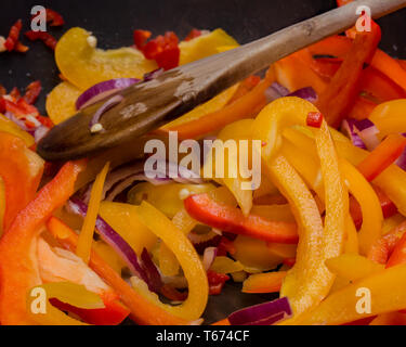 Cipolla rossa affettata (Allium cepa), tritato peperoncino (capsicum) e tritate il peperone giallo per la cottura in una padella antiaderente sul piano cottura Foto Stock