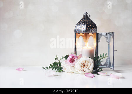 Messaggio di saluto festivo card, invito per vacanza musulmana del Ramadan Kareem.Vintage lanterna marocchina con la candela incandescente, rami verdi, le rose rosa fiori Foto Stock