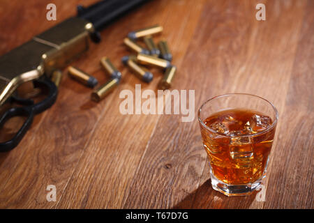 Wild West fucile e munizioni con un bicchiere di whisky e ghiaccio sulla barra di legno tabella Foto Stock