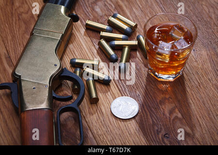 Wild West fucile e munizioni con un bicchiere di whisky e ghiaccio con il vecchio silver dollar sulla barra di legno tabella Foto Stock