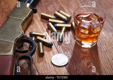 Wild West fucile e munizioni con un bicchiere di whisky e ghiaccio con il vecchio silver dollar sulla barra di legno tabella Foto Stock