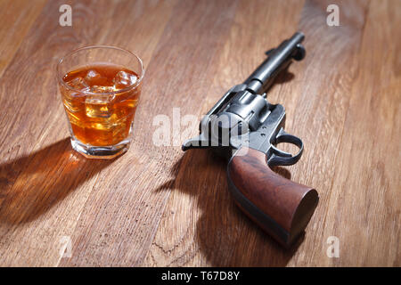 Wild West revolver e munizioni con un bicchiere di whisky e ghiaccio sulla barra di legno tabella Foto Stock