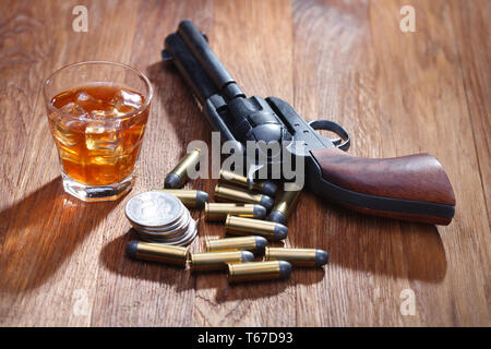 Wild West revolver e munizioni con un bicchiere di whisky e ghiaccio con il vecchio silver dollar sulla barra di legno tabella Foto Stock