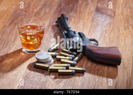 Wild West revolver e munizioni con un bicchiere di whisky e ghiaccio con il vecchio silver dollar sulla barra di legno tabella Foto Stock