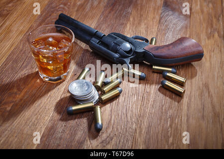 Wild West revolver e munizioni con un bicchiere di whisky e ghiaccio con il vecchio silver dollar sulla barra di legno tabella Foto Stock