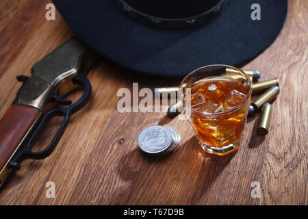 Wild West fucile e munizioni con un bicchiere di whisky e ghiaccio con il vecchio silver dollar sulla barra di legno tabella Foto Stock