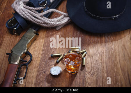 Wild West fucile e munizioni con un bicchiere di whisky e ghiaccio con il vecchio silver dollar sulla barra di legno tabella Foto Stock