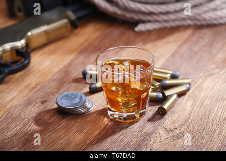 Wild West fucile e munizioni con un bicchiere di whisky e ghiaccio con il vecchio silver dollar sulla barra di legno tabella Foto Stock