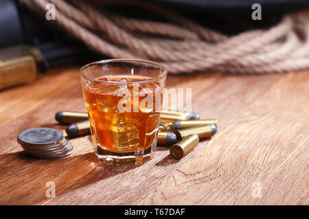 Wild West fucile e munizioni con un bicchiere di whisky e ghiaccio con il vecchio silver dollar sulla barra di legno tabella Foto Stock