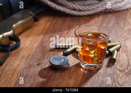 Wild West fucile e munizioni con un bicchiere di whisky e ghiaccio con il vecchio silver dollar sulla barra di legno tabella Foto Stock