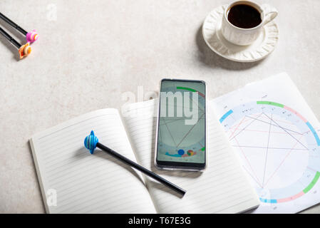 Aprire il notebook per la scrittura di idee e di nascita astrologico Natal grafico posa su uno sfondo grigio. Il caffè e il pianeta le penne nelle vicinanze. Vista dall'alto. Idea di Astrol Foto Stock