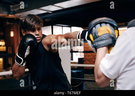 Giovane maschio boxer praticando fori in palestra con pullman Foto Stock