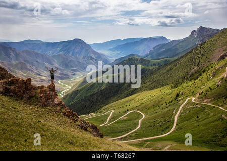 Un uomo si erge sul bordo di una scogliera. Una vista del pass e la magnifica valle, lungo la quale la strada syrpantin va. Kirghizistan Foto Stock