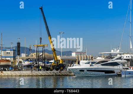 CANNES, Francia - Aprile 2019: gru mobile in cantiere nel porto di Cannes il sollevamento di un gommone con motore fuoribordo nell'acqua. Foto Stock