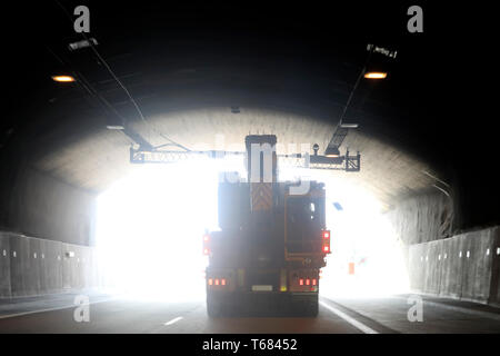 Semi rimorchio trasporta un carico oversize contro la luce del giorno alla fine di un tunnel di freeway. Foto Stock