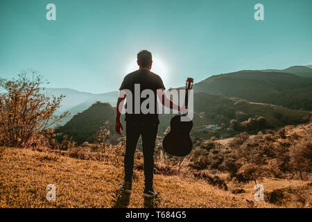 Uomo con chitarra in montagna in una giornata di sole Foto Stock