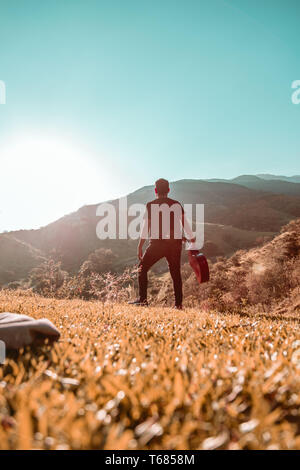 Uomo con chitarra in montagna in una giornata di sole Foto Stock