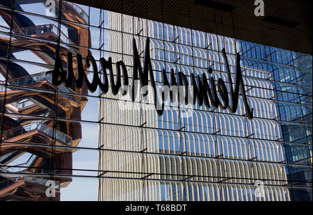 Sulla sinistra il temporaneo nave scultura in acciaio con persone in piedi su di esso, visibile dall'interno della Hudson Yards mall, shot attraverso il retro di un Neiman Marcus segno nella finestra di un edificio in costruzione a destra. L'interactive nuovo segno distintivo composto da interconnessi rampe di scale è stato progettato da architetto britannico Thomas Heatherwick come punto focale dei nuovi cantieri di Hudson complesso, che ha debuttato il 15 marzo 2019, a controversie circa il fatto che esso era troppo elitario. Lo sviluppo comprende retail residenziale, di ristoranti e di istituzioni culturali e spazi pubblici. Foto Stock